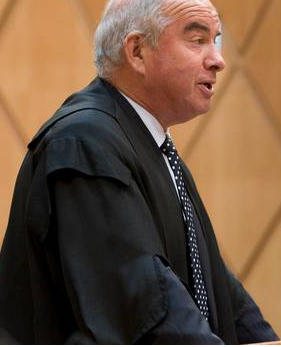 Colin Carruthers QC, grey-haired and wearing barrister's robes over a suit, speaking in a courtroom.