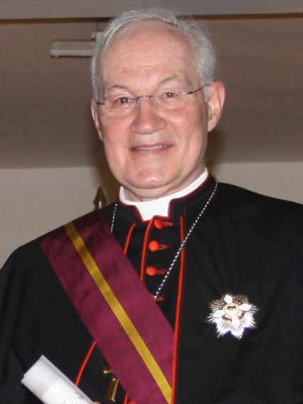 Cardinal Marc Ouellet, photographed from the chest up in black clerical dress with red trim and a maroon ceremonial sash, wearing rimless glasses and looking towards the camera.