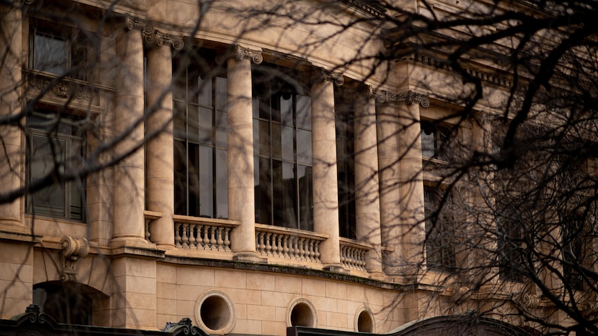 Bare winter branches in front of the sandstone facade of Adelaide's District Court, with tall columns and arched windows.