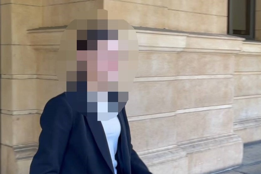 A woman in a dark blazer and white top walking past a sandstone court building, her face pixellated.