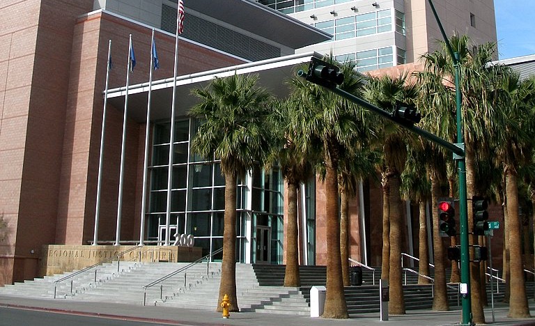 The entrance of the Regional Justice Center in downtown Las Vegas, with wide stone steps, flagpoles and a row of tall palm trees in front of a glass-fronted lobby.