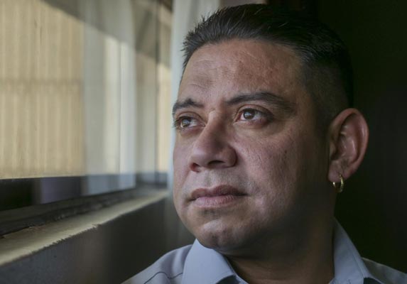 Clemente Aguirre-Jarquin, a man with short dark hair and a small gold earring, gazes toward a window, light falling across his face.