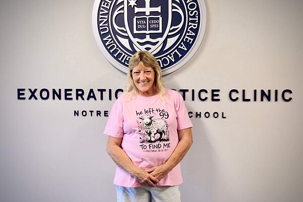 Iris Seabolt stands smiling in front of a wall sign reading Exoneration Justice Clinic, Notre Dame Law School.