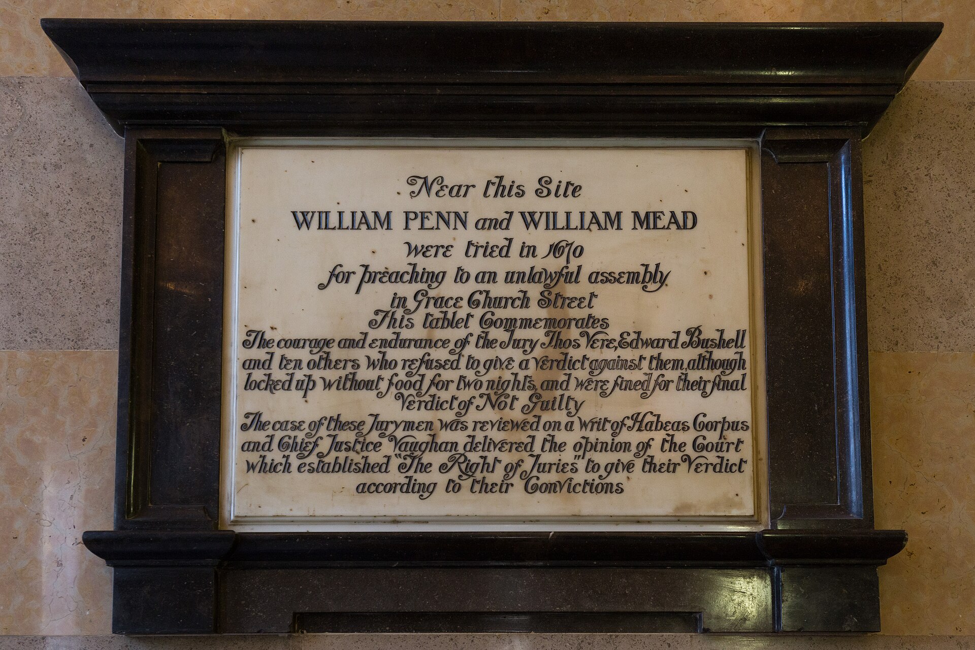 The William Penn and William Mead tablet inside the Old Bailey, a marble panel in a dark wooden surround, its calligraphic inscription commemorating the jury who refused to convict them in 1670 and the ruling that established the right of juries to give their verdict according to their convictions.