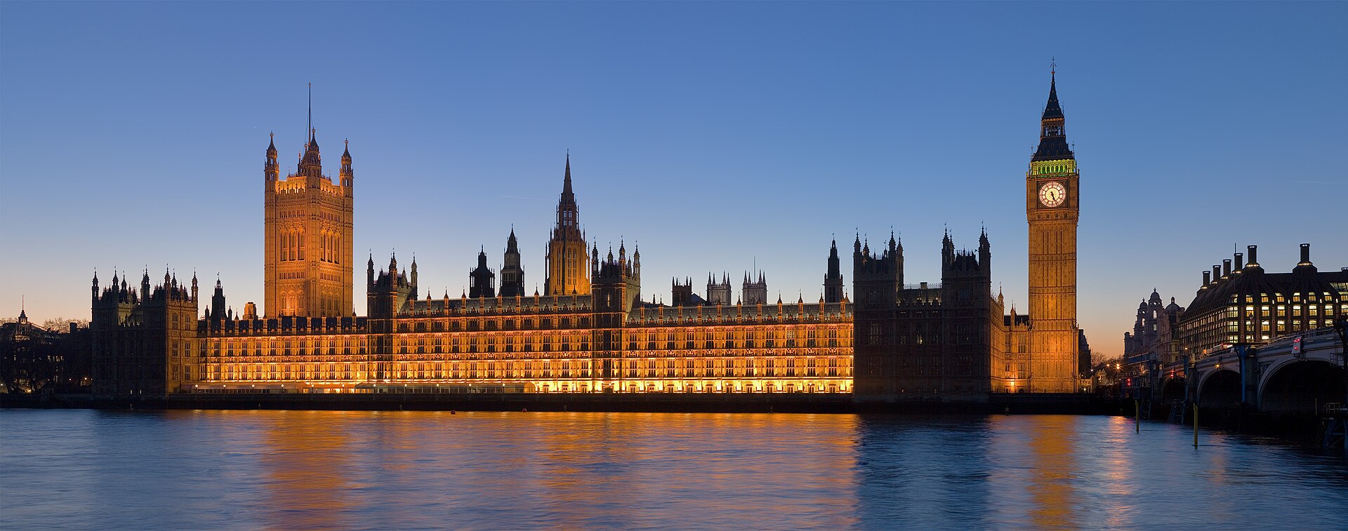The Palace of Westminster and Elizabeth Tower lit up at dusk, seen across the River Thames