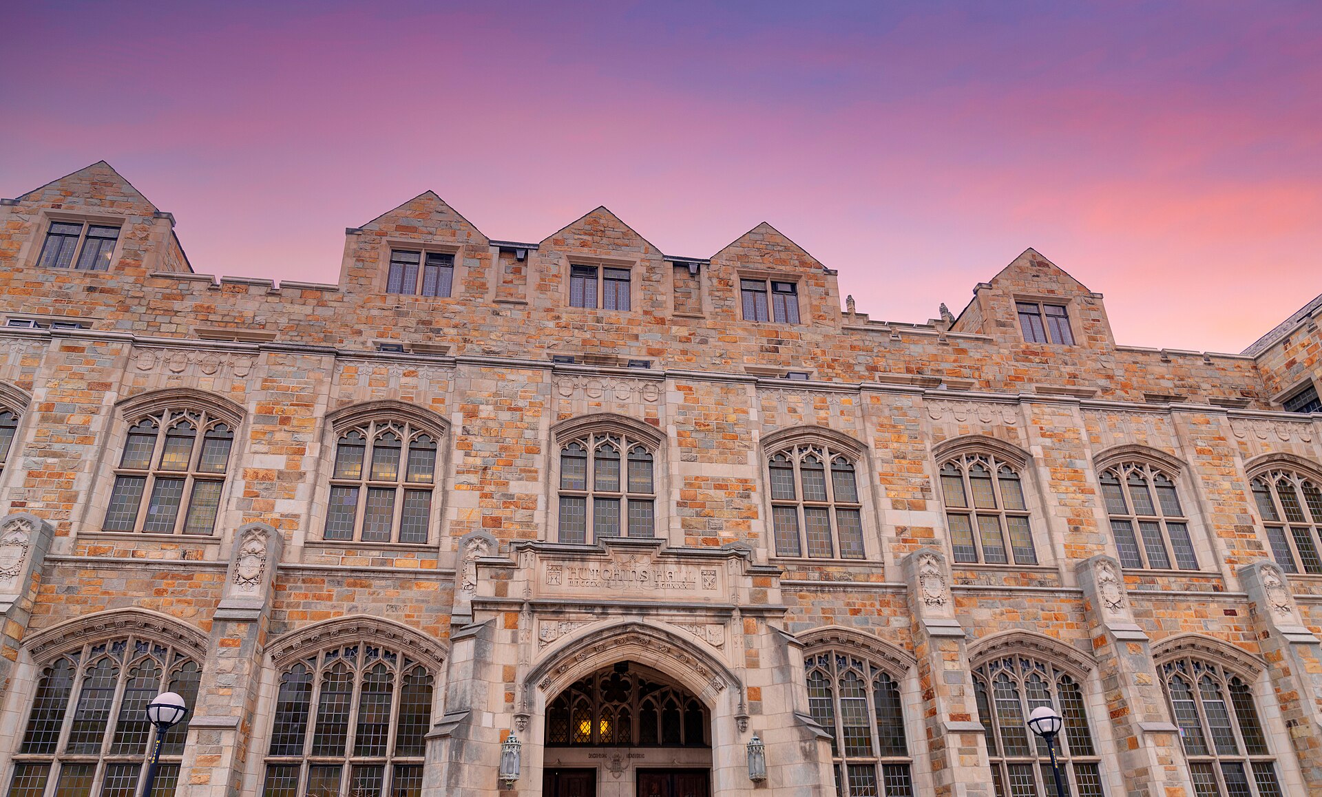 The stone Gothic facade of Hutchins Hall at the University of Michigan Law School in Ann Arbor, under a pink evening sky