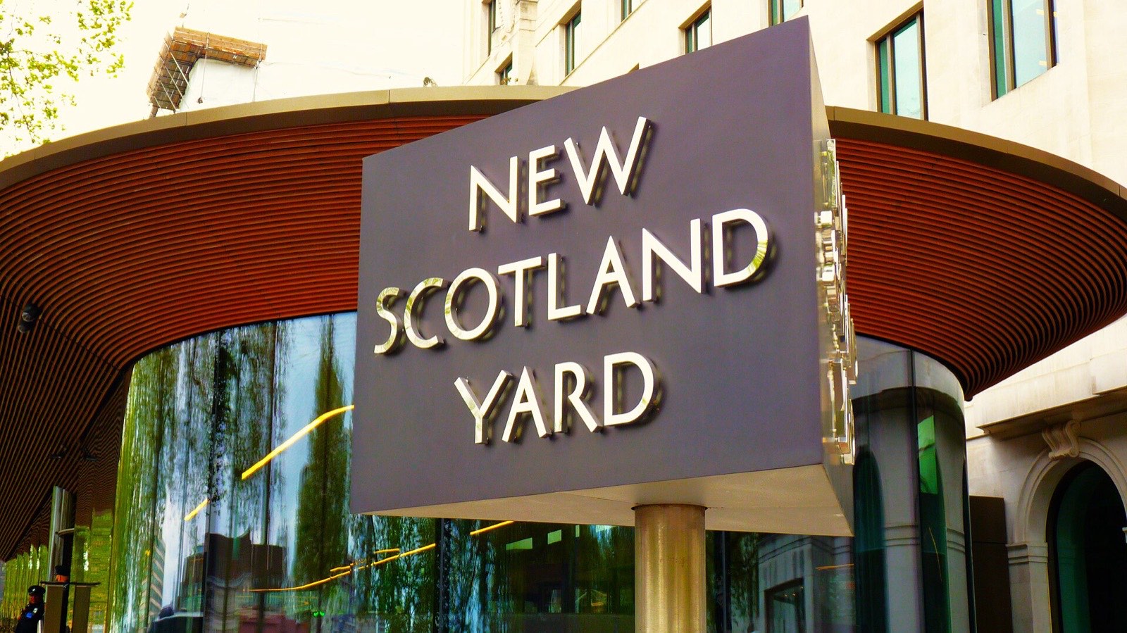The revolving New Scotland Yard sign outside the Metropolitan Police headquarters in Victoria, London, with the building's curved bronze fins behind it.