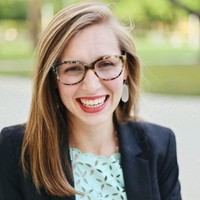 Headshot of Madison Reddick Smyser, smiling, in tortoiseshell glasses and a dark blazer