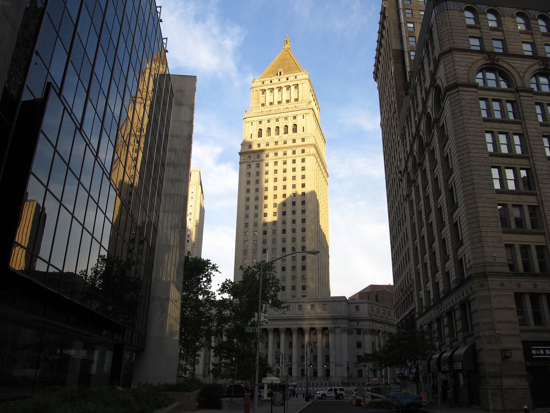 The gilded pyramid-topped tower of the Thurgood Marshall US Courthouse rising above its colonnaded base at the end of a Manhattan street, lit by low sun between dark office buildings.