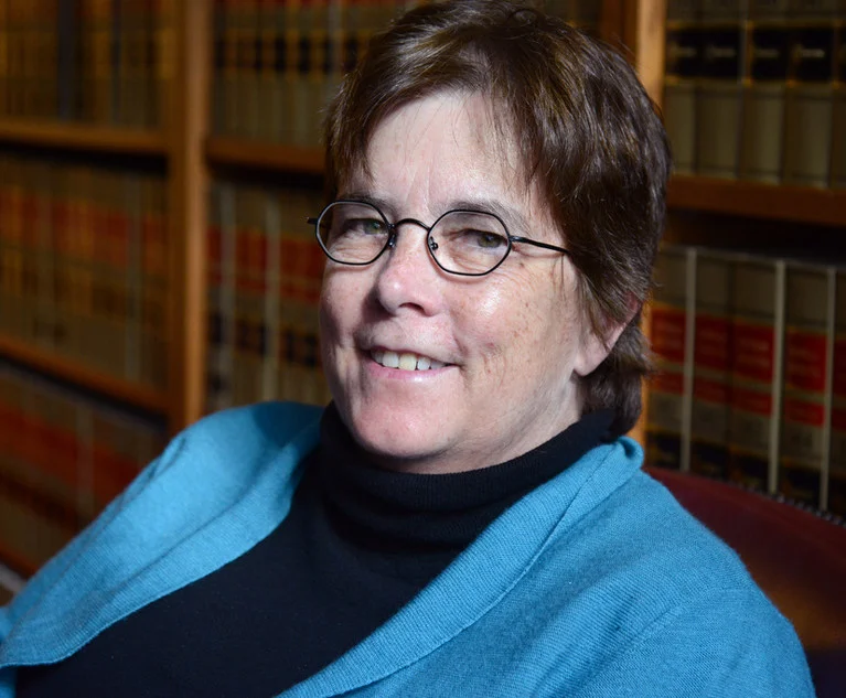 Judge Valerie Caproni, smiling, in glasses and a blue wrap, in front of shelves of law books