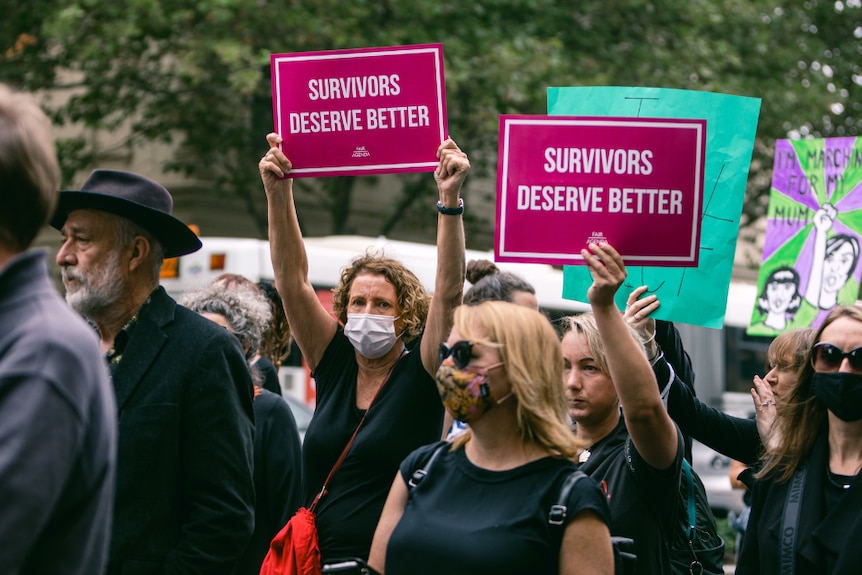 Protestors hold up signs which read "Survivors deserve better".