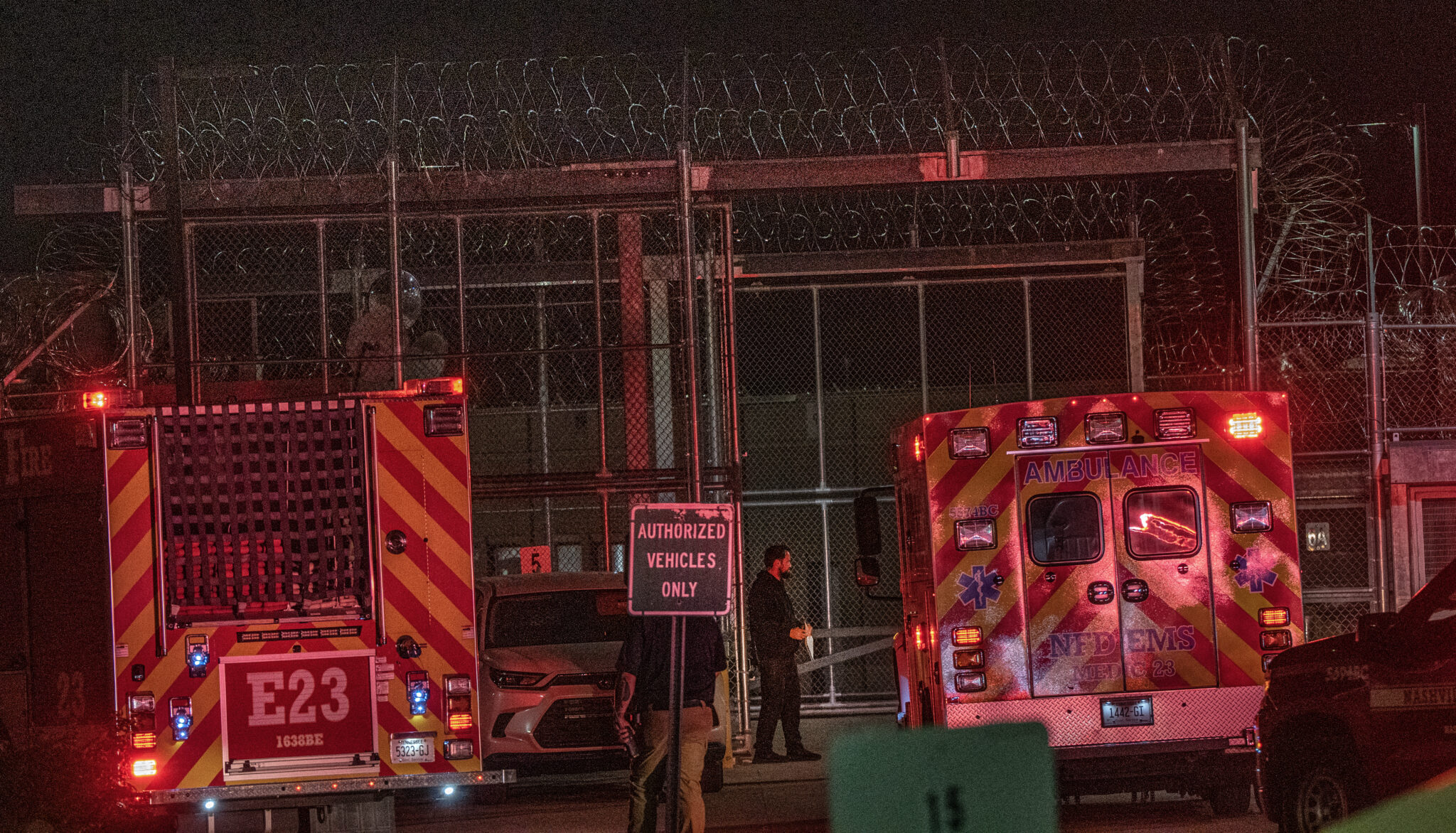 A fire engine and an ambulance with lights on outside the razor-wire fence of Riverbend Maximum Security Prison at night