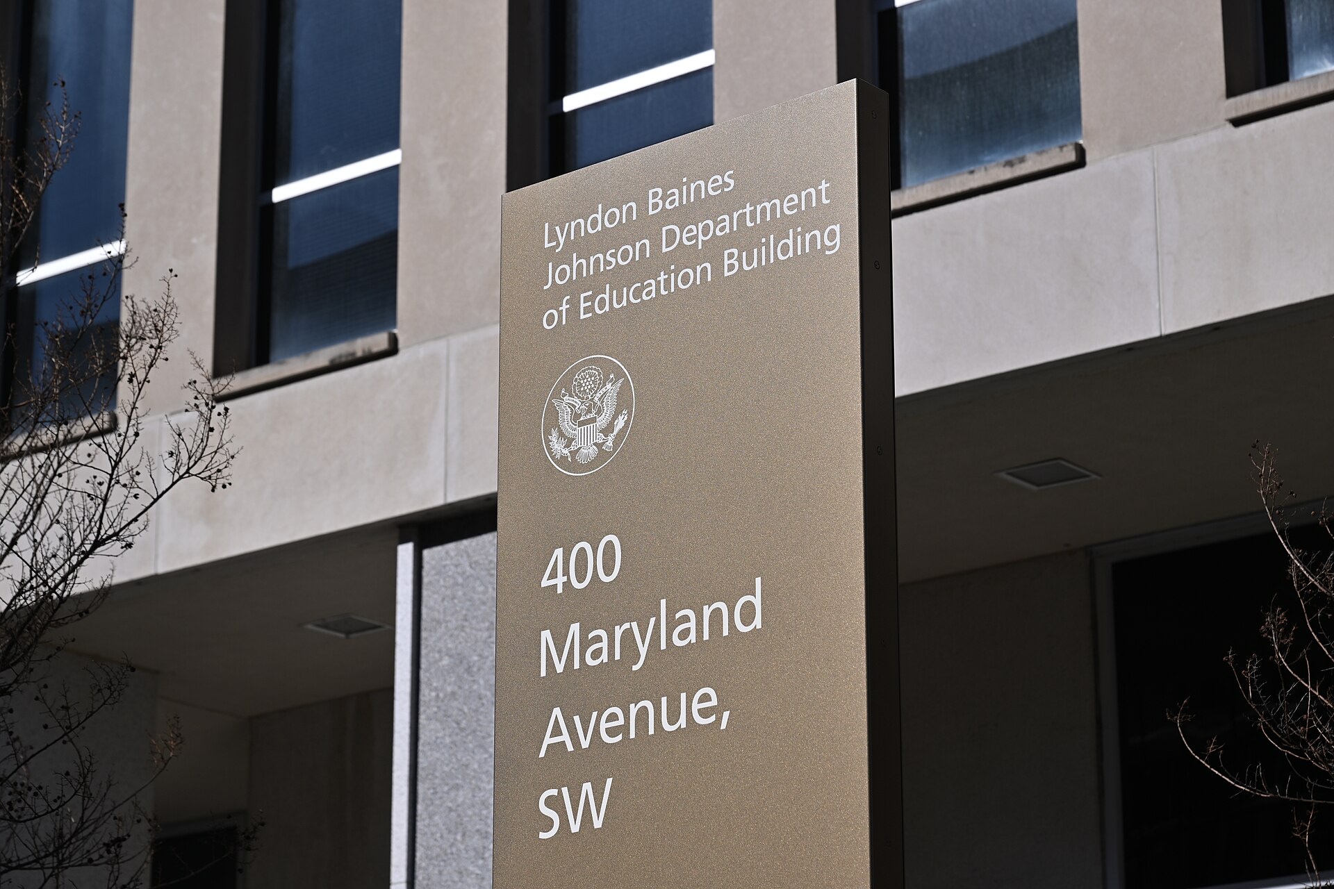 A tall bronze-coloured sign reading 'Lyndon Baines Johnson Department of Education Building, 400 Maryland Avenue, SW', with the US government seal, in front of the building's stone facade.