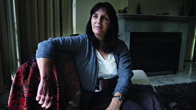 Cathy Kezelman seated in an armchair in her living room, one arm along the chair back, a stone fireplace behind her.