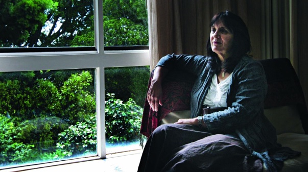 Cathy Kezelman seated in an armchair beside a large window, looking out over a green garden.