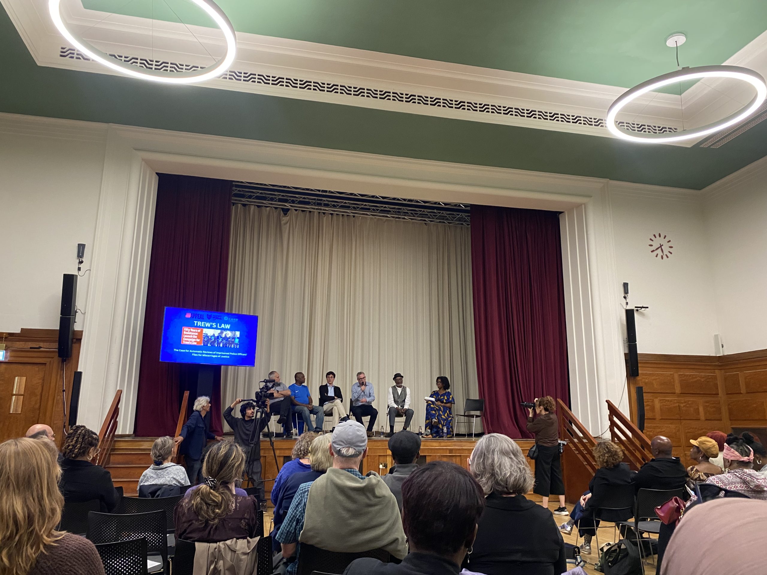 Panellists seated on stage at the Trew's Law campaign launch in Lambeth Town Hall, addressing a full audience beneath a screen reading 'Trew's Law'.