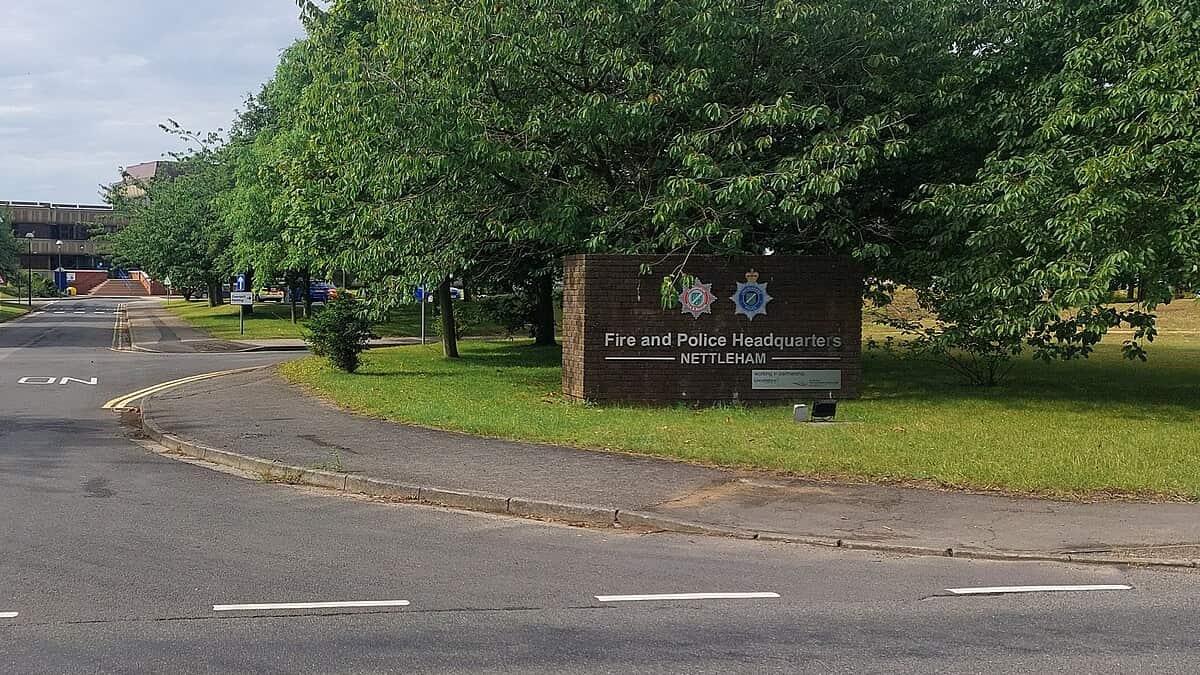 The entrance sign at Lincolnshire Fire and Police Headquarters in Nettleham, carrying the Lincolnshire Police and fire service crests, with the headquarters building visible beyond the trees.